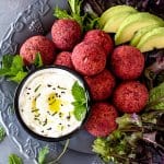 Falafel with red beetroot piled up on a plate with lettuce and yogurt sauce.
