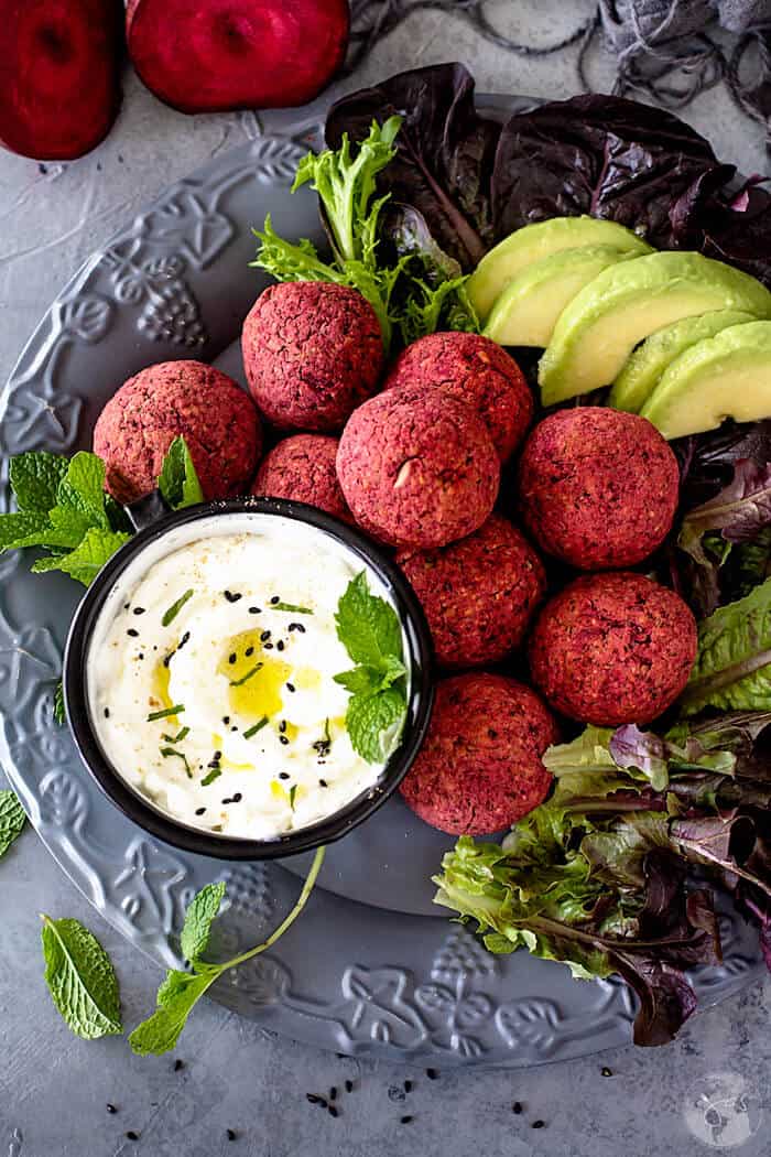 Falafel with red beetroot piled up on a plate with lettuce and yogurt sauce.