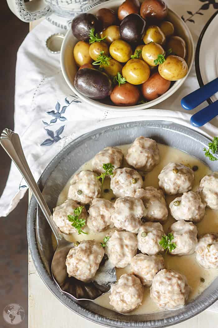A flat lay of the meatballs served with a spoon and a bowl of fingerling potatoes.