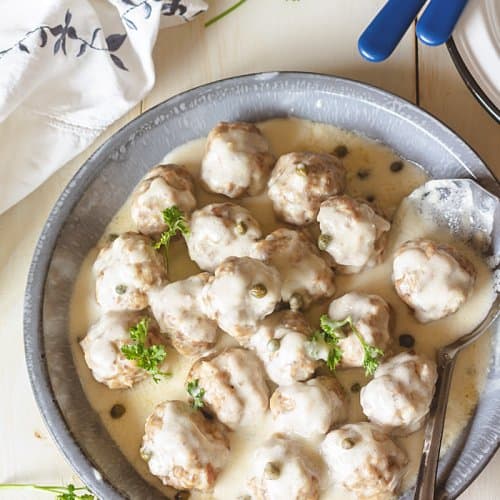 An overhead shot of German meatballs with gray bowl on rustic white wooden background