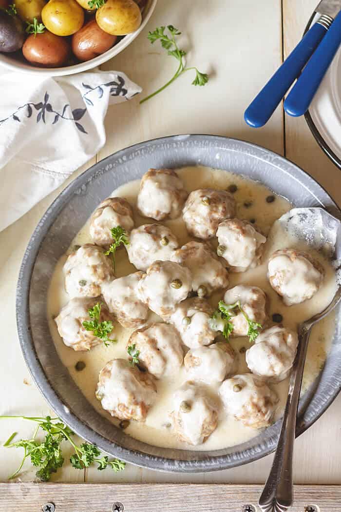 An overhead shot of German meatballs with gray bowl on rustic white wooden background