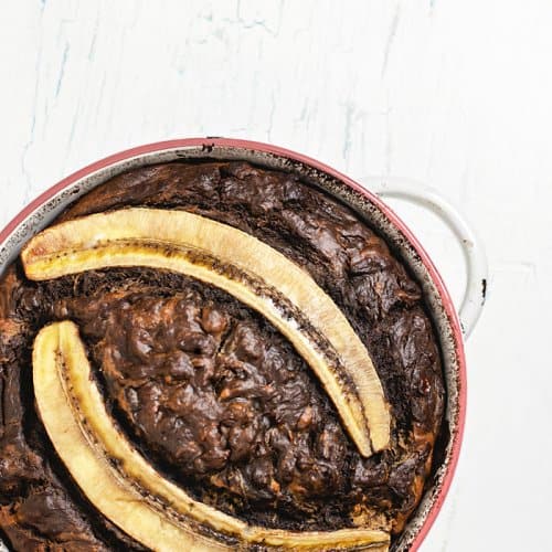 A round pan with chocolate banana bread topped with two banana halves on a white counter.