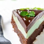 A close up of a mint chocolate cake slice with mint leaves and sprinkles.