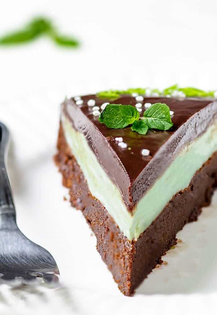 A close up of a mint chocolate cake slice with mint leaves and sprinkles.