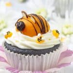 Adorable apricot bee sitting on top of cream cheese frosted chocolate cupcake.