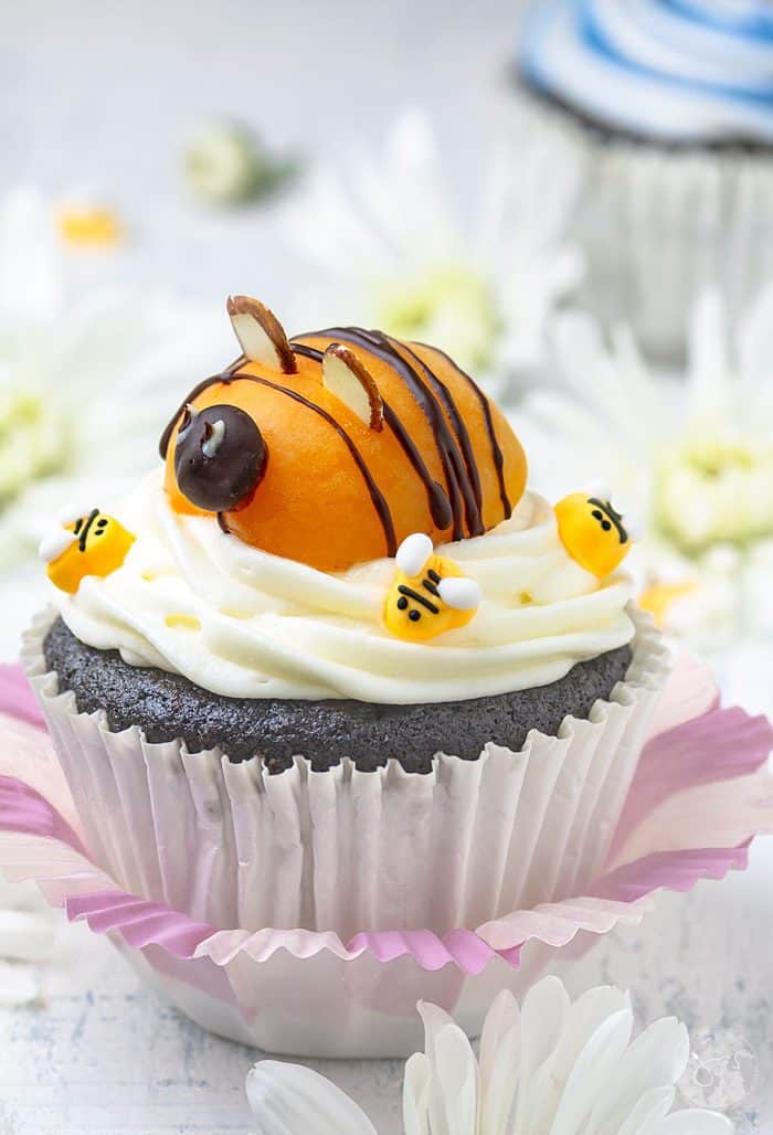 Adorable apricot bee sitting on top of cream cheese frosted chocolate cupcake.