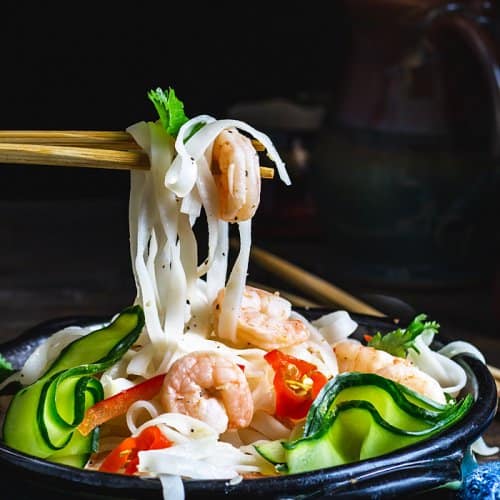 Rice noodles and shrimp on chopsticks over the Thai salad bowl.