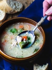 A spoonful of soup dipped into the bowl showing chicken, carrot, and okra.