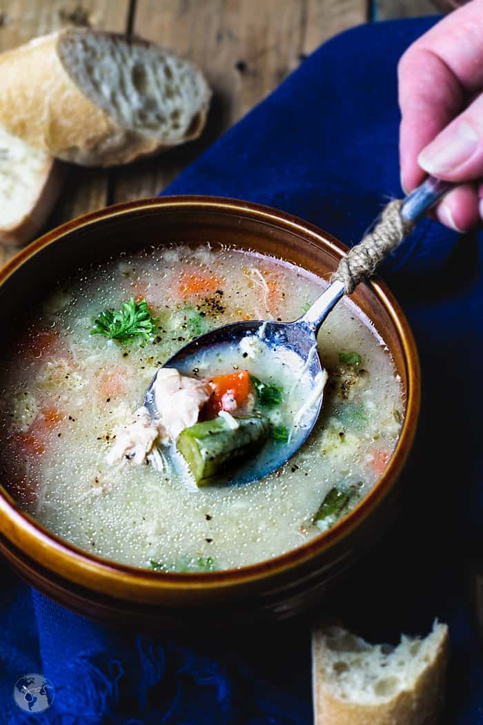 A spoonful of soup dipped into the bowl showing chicken, carrot, and okra.