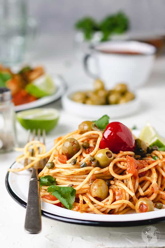 A plate piled up with spaghetti on a white table and a cup