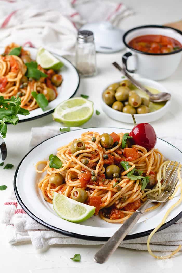 Veracruz salsa, spaghetti, lime, and olives on a table.