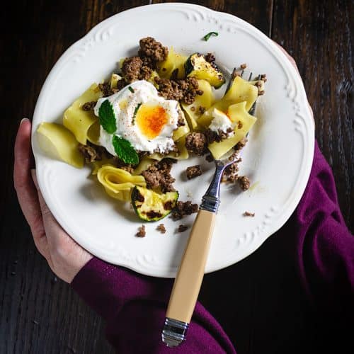 A person setting a plate of Turkish pasta dish on the table.