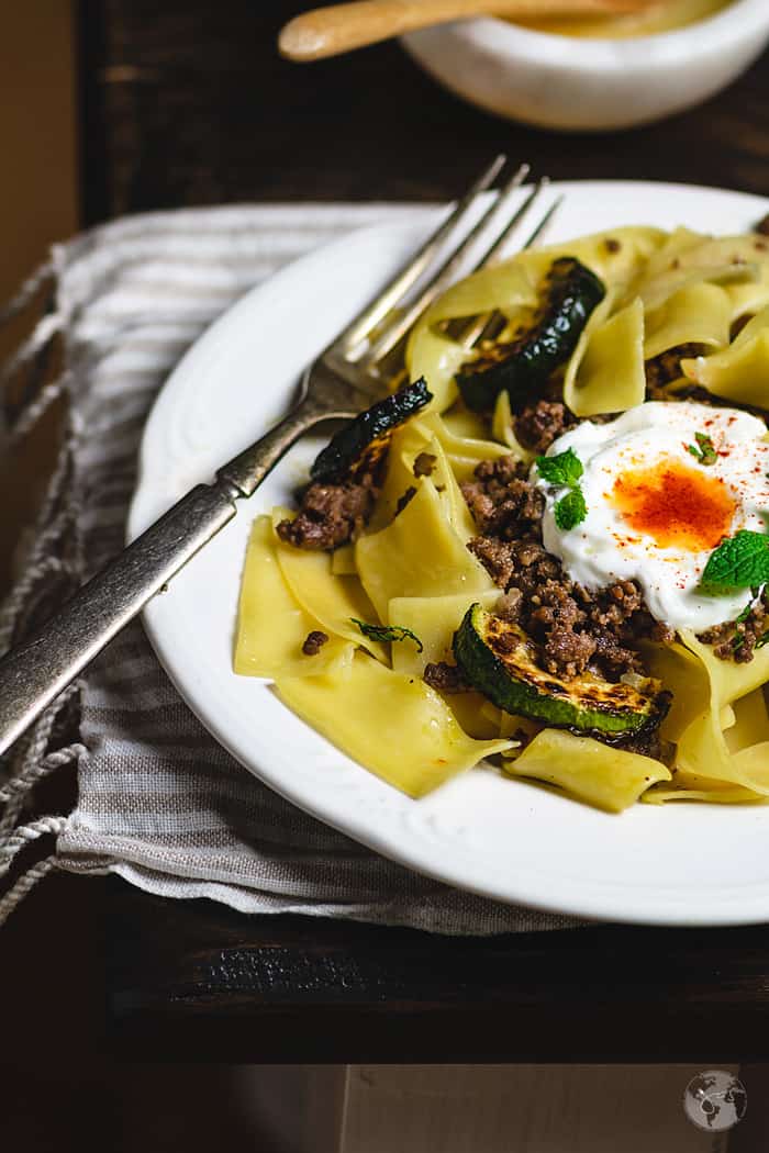 Close up of the white plate with wide egg noodles topped with cooked ground lamb and yogurt with a fork on the side.