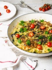 Pasta frittata in a white skillet with cherry tomatoes