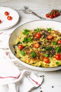 Pasta frittata in a white skillet with cherry tomatoes