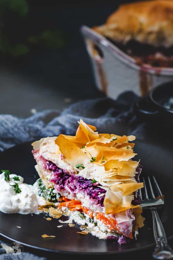 A moody shot of the slice of vegetable and cheese pie on a plate.