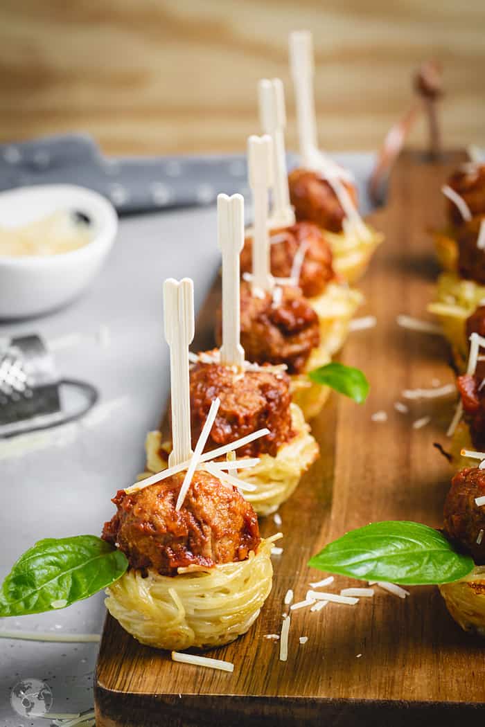 Meatball and spaghetti appetizer nests lined on a wooden board.