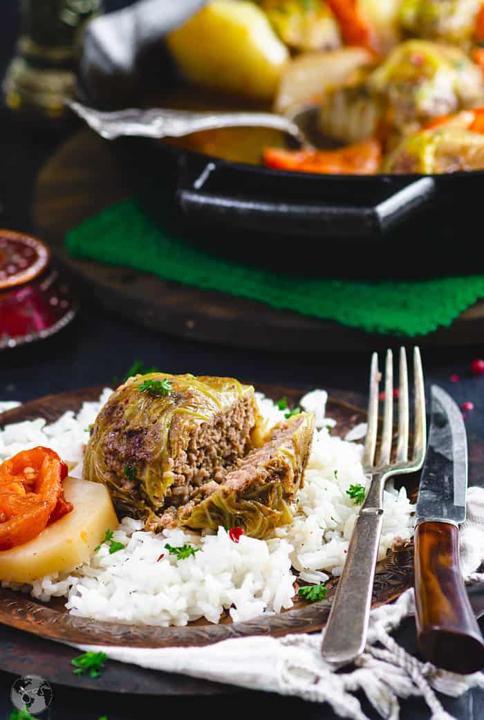 A sarmale roll served on a bed of white rice with the dish in the background. 