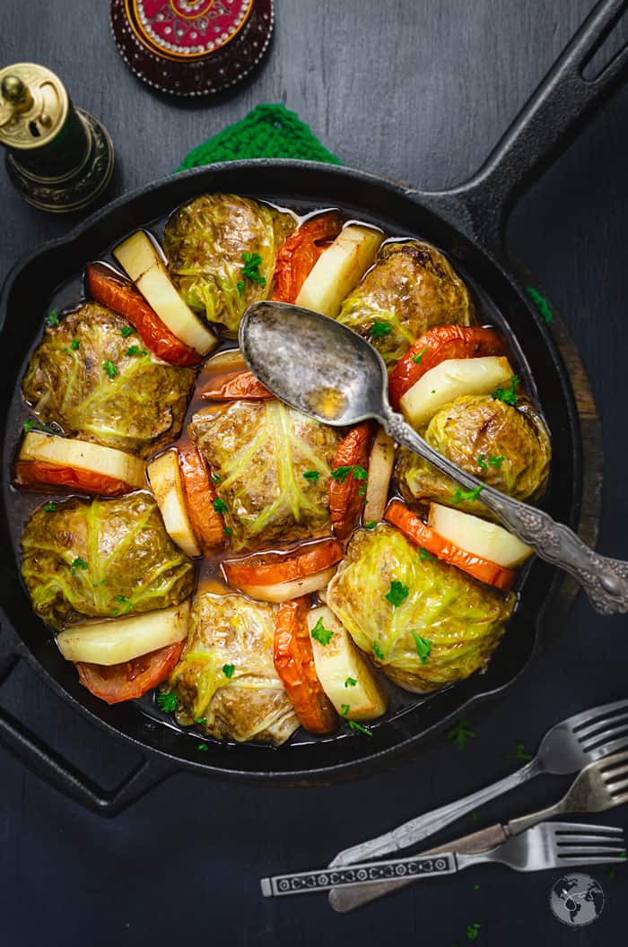 An overhead shot of Palestinian Stuffed Savoy Cabbage Rolls in a cast Iron skillet on a black background