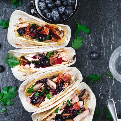 Four tacos lineup with turkey meat and a bowl with blueberries.