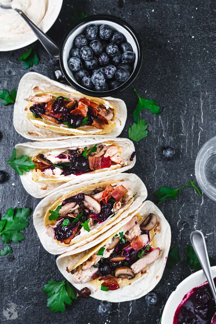 Four tacos lineup with turkey meat and a bowl with blueberries.