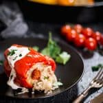 Pepper stuffed with potato with roasting pan and tomatoes in the background.