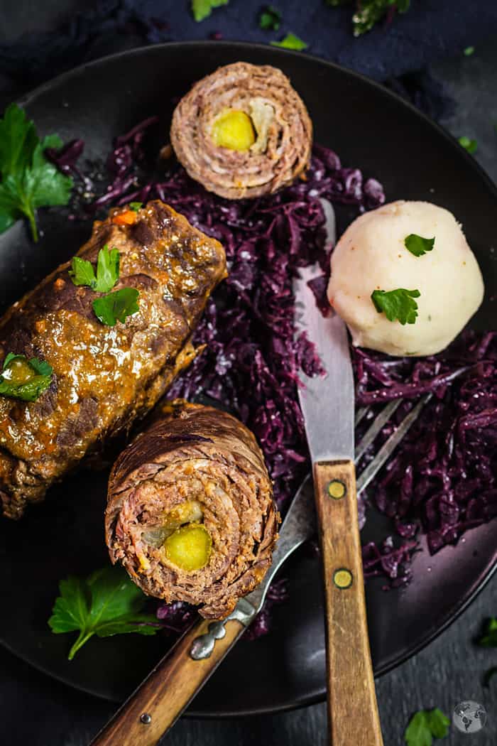 A close up shot of rouladen on a plate with rotkohl and a fork and knife