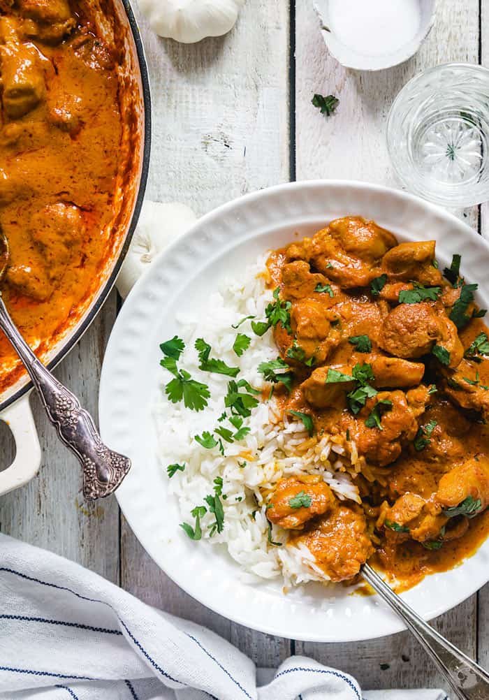 Orange-colored chicken tikka masala with rice in a white plate with white wooden background