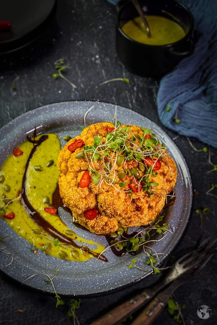 Easy to make oven-baked whole head of cauliflower, spiced with chili pepper and topped with pepitas and microgreens.