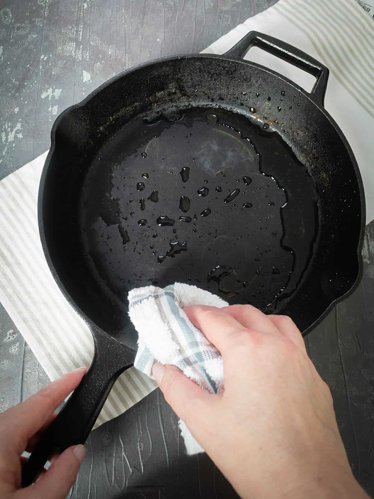 Wiping iron skillet with wet kitchen towel.
