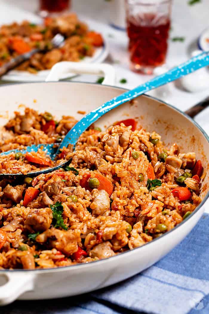 Rice with vegetables and pieces of chicken thighs in a white enamel cast-iron skillet