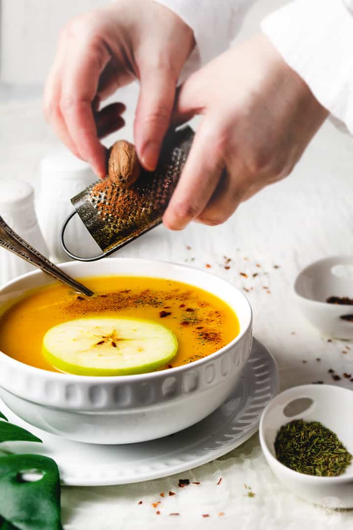 Grating a whole nutmeg over a bowl of squash soup