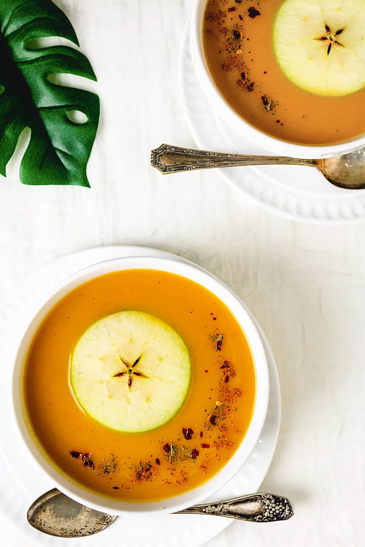 Two bowls of soup with spoons on a white tablecloth and green leaf