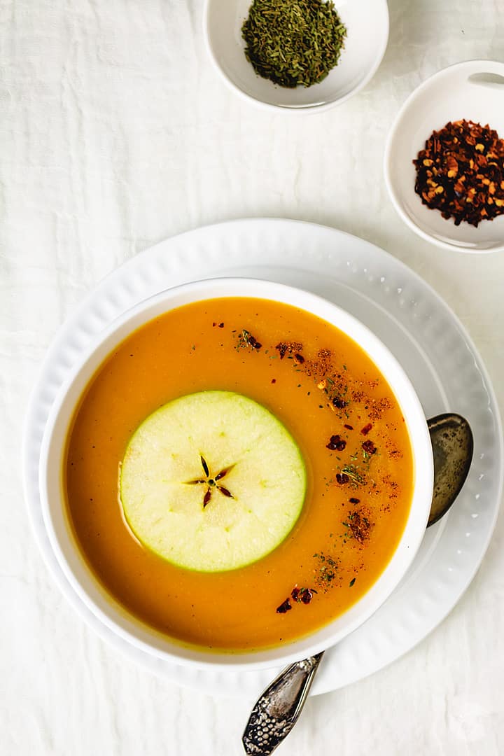 One serving of soup with small ramekins filled with spices. 