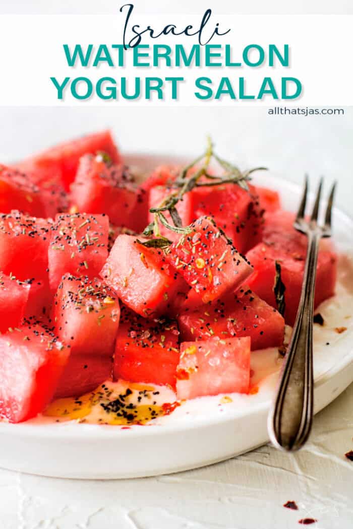 Angle shot of cubed watermelon over yogurt with rosemary in a white plate with text overlay.