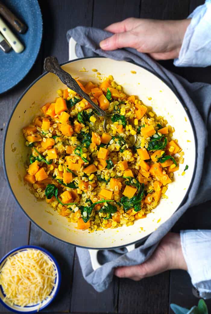 A skillet with barley and squash dish being placed on the table.