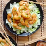 overhead shot of shrimp with bang bang sauce on a black plate and bamboo background