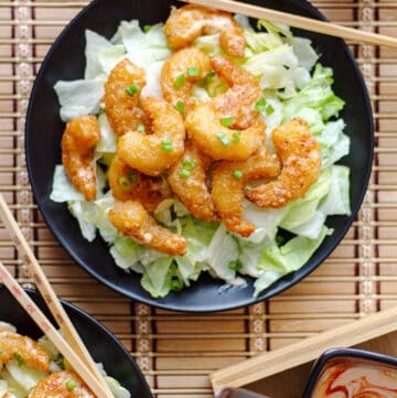 overhead shot of shrimp with bang bang sauce on a black plate and bamboo background