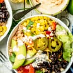 An overhead shot of assembled burrito bowl topped with avocado, jalapenos, black beans, corn, tomatoes, peppers, and lettuce.