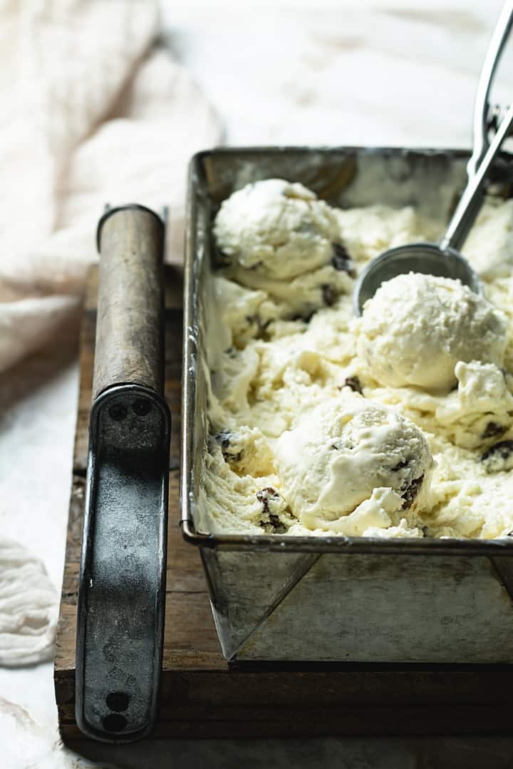 A shot of a loaf tin filled with no-churn rum and raisins gelato with ice cream scoop.