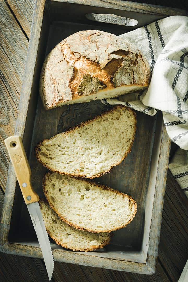 An overhead view of the sliced bread in a wooden box with a knife.