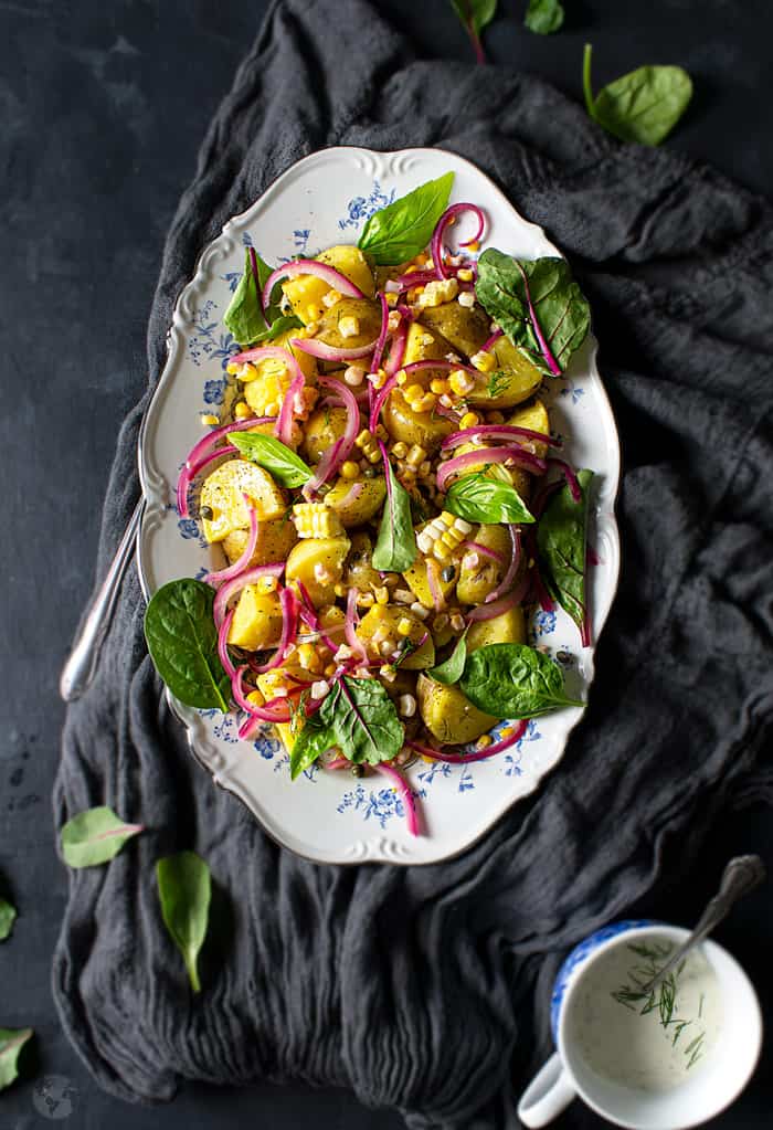 A salad with potatoes, corn, and baby greens in an oval serving plate on a gray cloth