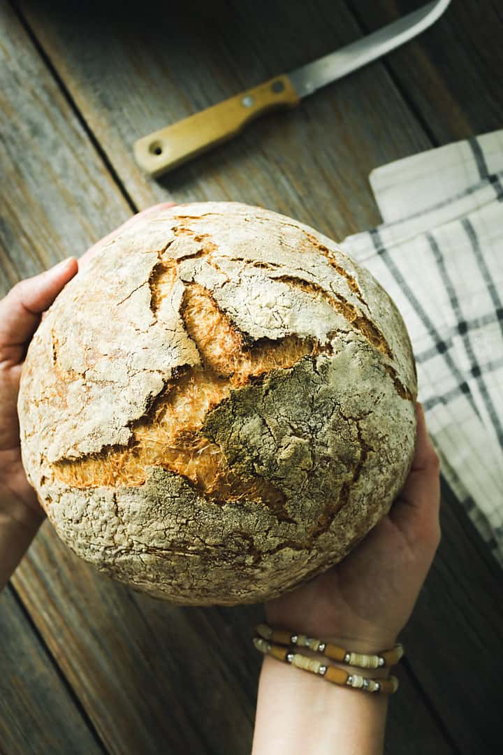 A flat lay of hands holding the artisan bread over the wooden background.