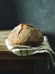 Straight-on shot of baked bread loaf on a kitchen towel, sitting on a rustic wooden table