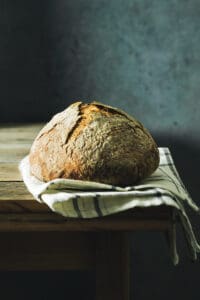 Straight-on shot of baked bread loaf on a kitchen towel, sitting on a rustic wooden table
