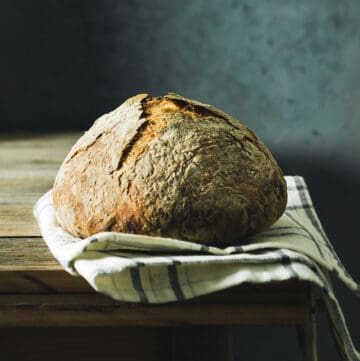 Straight-on shot of baked bread loaf on a kitchen towel, sitting on a rustic wooden table