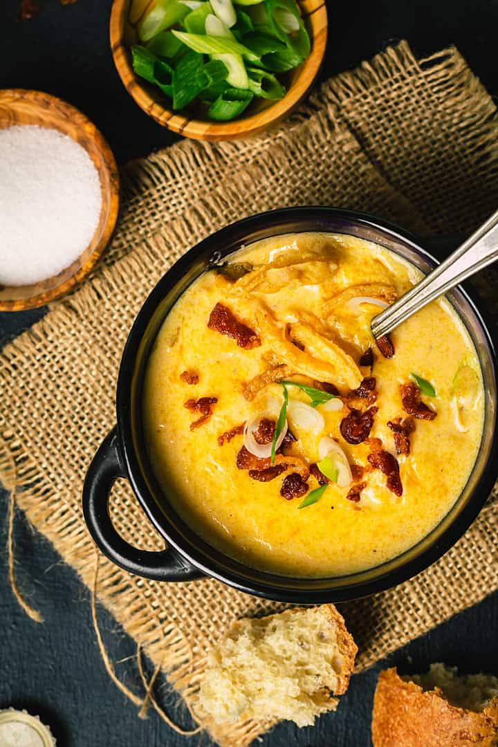 A flat lay of the cheesy soup in a black mini pot served with a spoon on a folded jute.