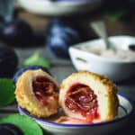 A front shot of the plum dumpling sliced in half with plums and sugar dish in the background