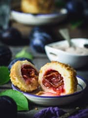 A front shot of the plum dumpling sliced in half with plums and sugar dish in the background