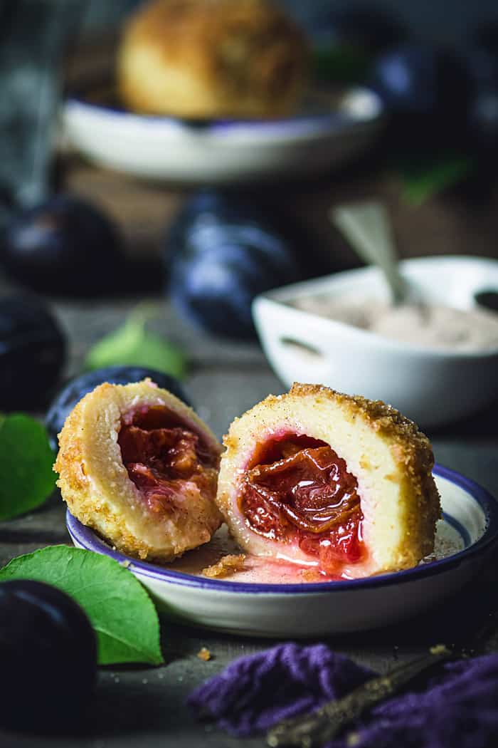 A front shot of the plum dumpling sliced in half with plums and sugar dish in the background